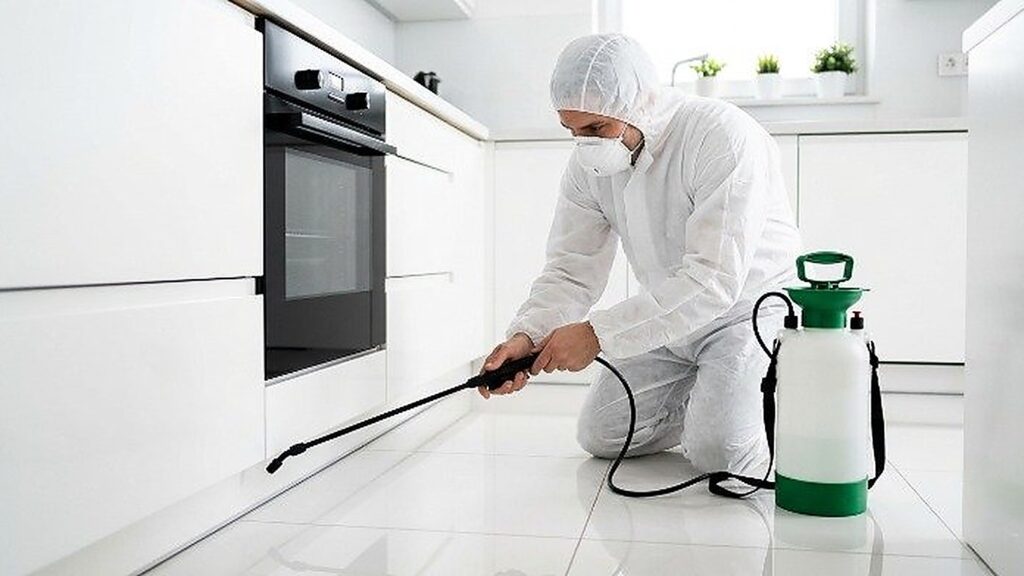 Professional pest control technician in white uniform spraying kitchen floor for pest treatment in Southlake, TX